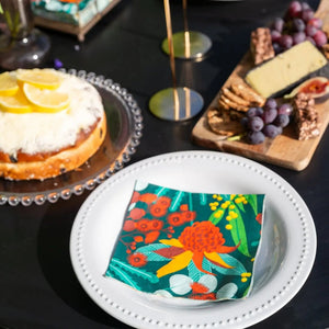 Allgifts Australia paper napkins featuring a vibrant Australian botanical print on a white plate at a table setting.